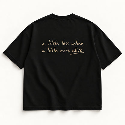 Schwarzes More Alive Tee, Rücken mit champagnerfarbener Handschrift „a little less online, a little more alive.“