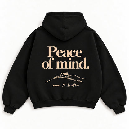 Schwarzer Peace of Mind Hoodie von hinten mit champagnerfarbenem Schriftzug und kleiner Hütte in einer Hügellandschaft